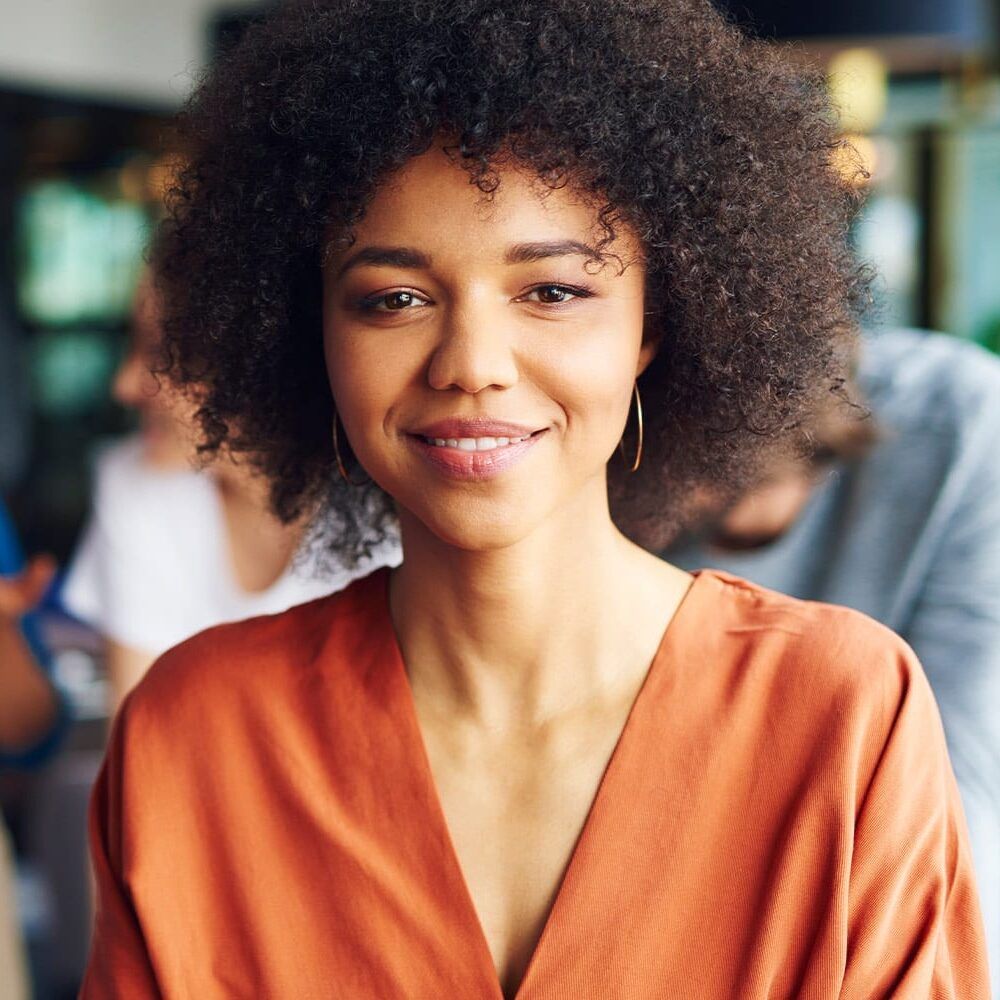 Person with curly hair and an orange shirt smiling at the camera