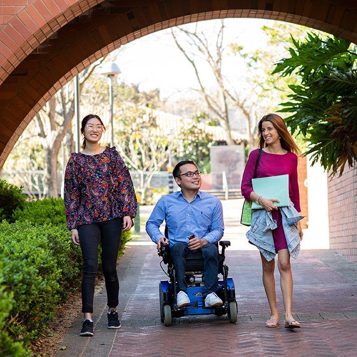 Three people, one in a wheelchair, walking on campus