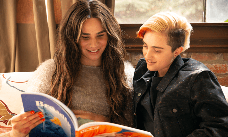 A transfeminine non-binary person and transmasculine gender-nonconforming person reading a magazine together