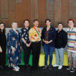 A group of people, including the IDAHOBIT panellists and organisers, stand together in front of a wall, smiling