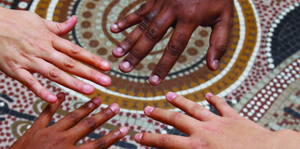 Hands touching over an aboriginal dot painting