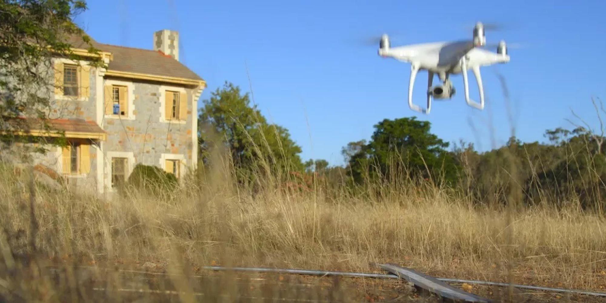 A drone flying in a field with a house to the left - play video