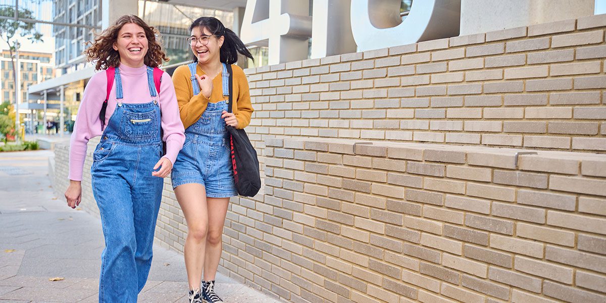 Two girls walking and laughing through campus