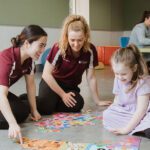 Two female OTs working with small smiling girl.