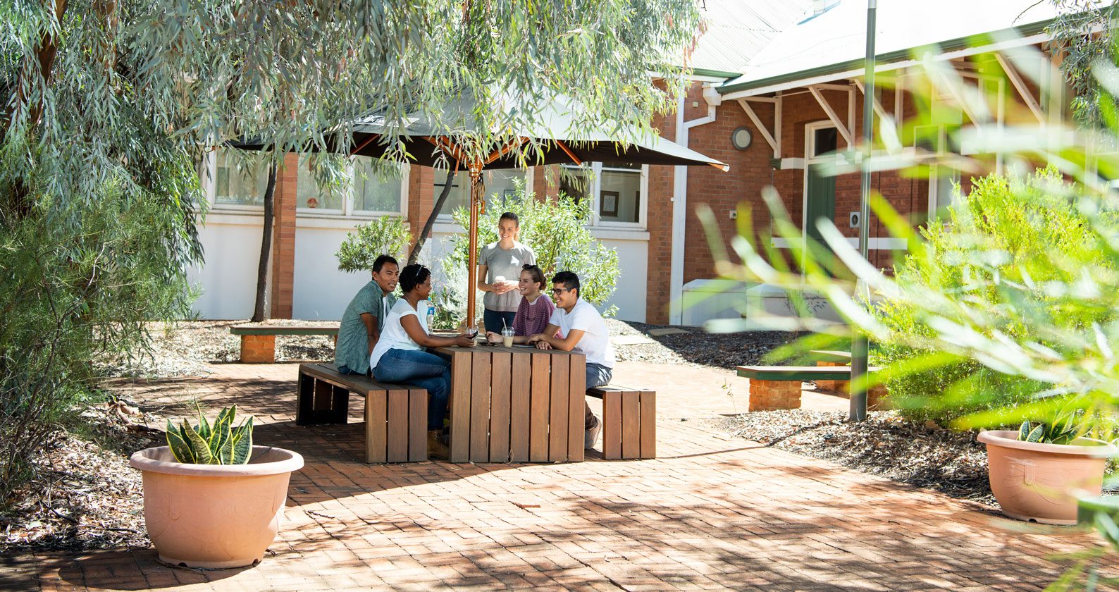 A group of students sitting at a table underneath an umbrella on the Curtin Kalgoorlie campus.