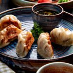 side view of traditional asian dumplings with meat and vegetables served with soy sauce on a plate on rustic background.