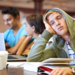 Student sitting at table surrounded by books and empty coffee cups.