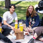 Four student sit on a rug at the Creative Quarter around a table with bubble tea. They smile at the camera.