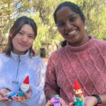 Two students stand outdoors holding painted gnomes.