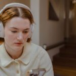 Student looks disappointed. She wears headphones and stares down at her phone.