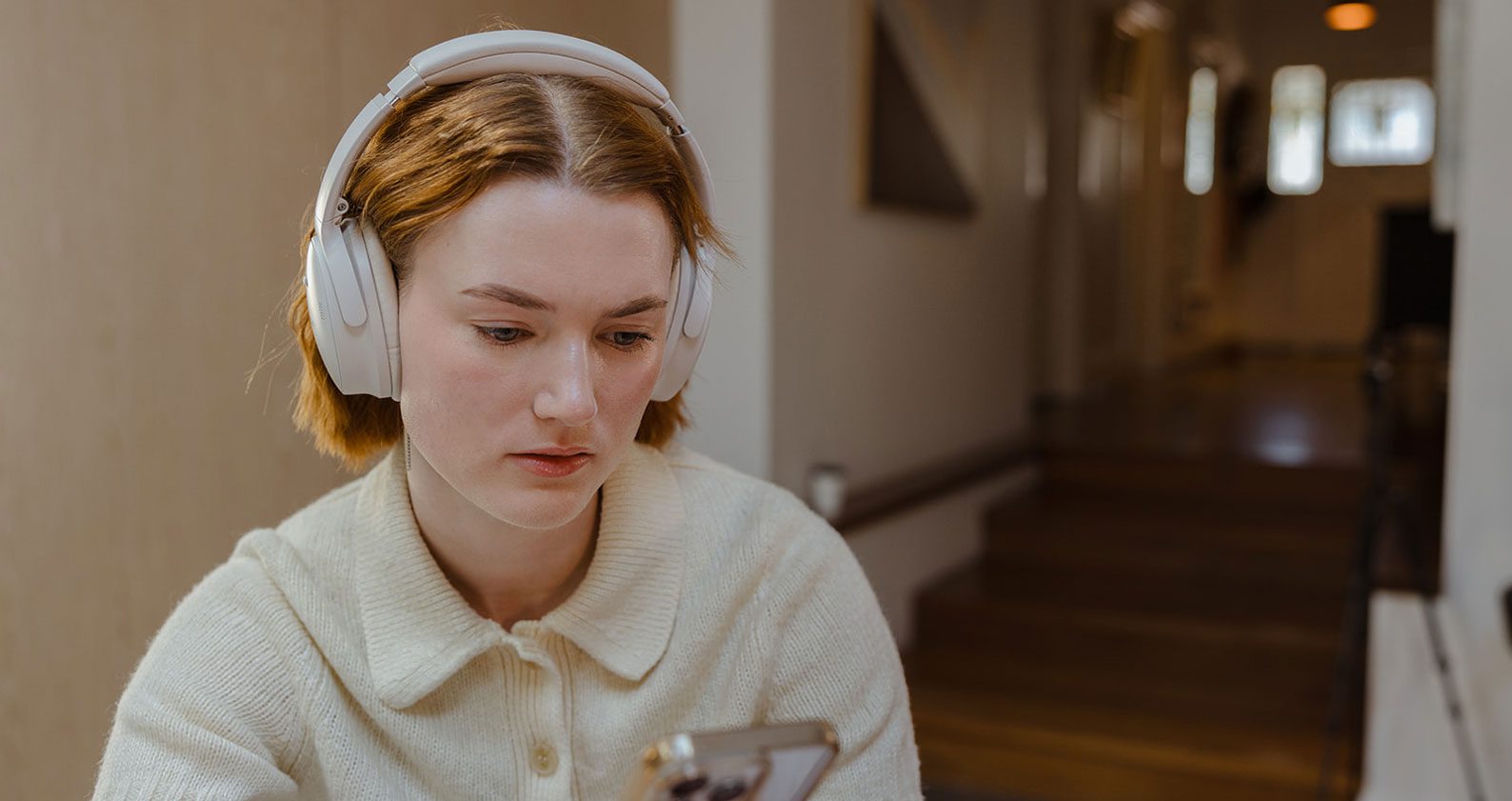 Student looks disappointed. She wears headphones and stares down at her phone.