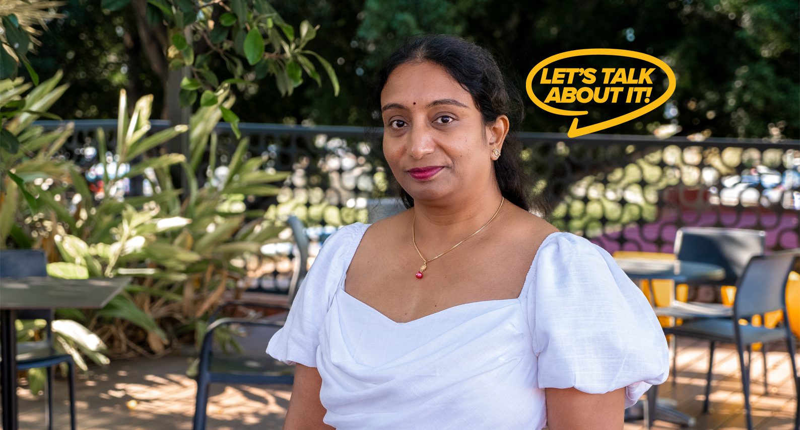 Yamini a mature aged student smiles wearing a white dress and red lipstick.