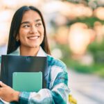 A student holding books and smiling into the distance.