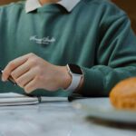 A student holding a pen above a notebook. There is a croissant to the side of the image.