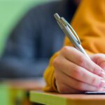 Student taking exam in classroom. Education test and literacy concept. Cropped shot, hand detail.