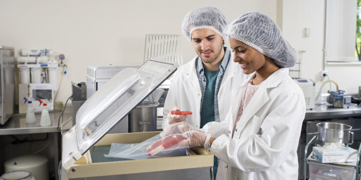 Two people very carefully lowering two steaks into a sou vide machine