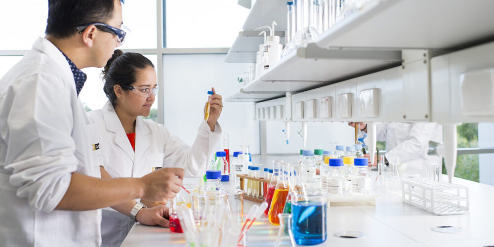 Two research students looking at colourful chemical glassware