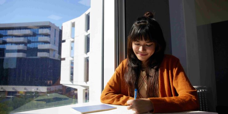 student smiling at her coursework near a window