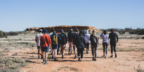 A group of people walking towards a large expanse of desert.