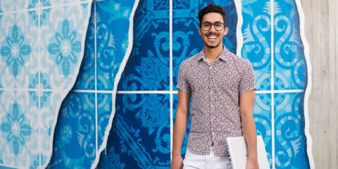 Student holding a white laptop in front of a blue wall