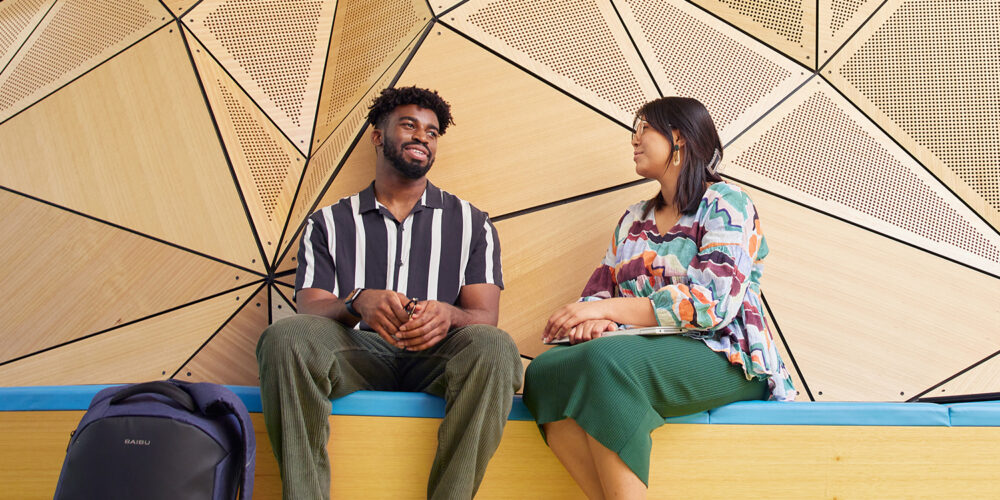 Two students sitting on a campus bench in conversation.