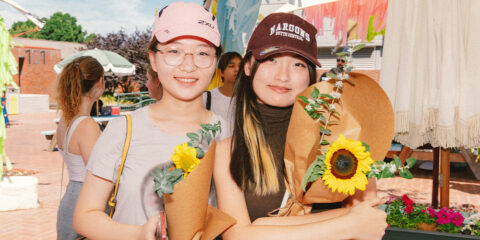 Two students wearing caps and holding sunflowers.