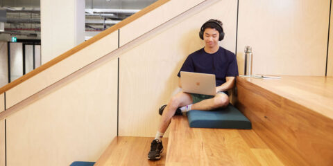 A student sits on the Library stairs and uses their laptop.