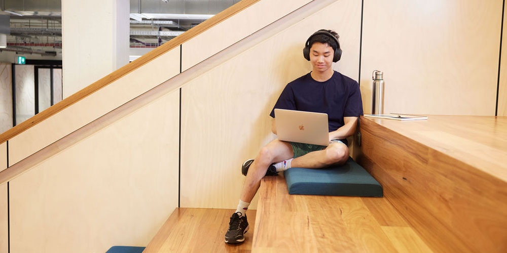 A student sits on the Library stairs and uses their laptop. - play video