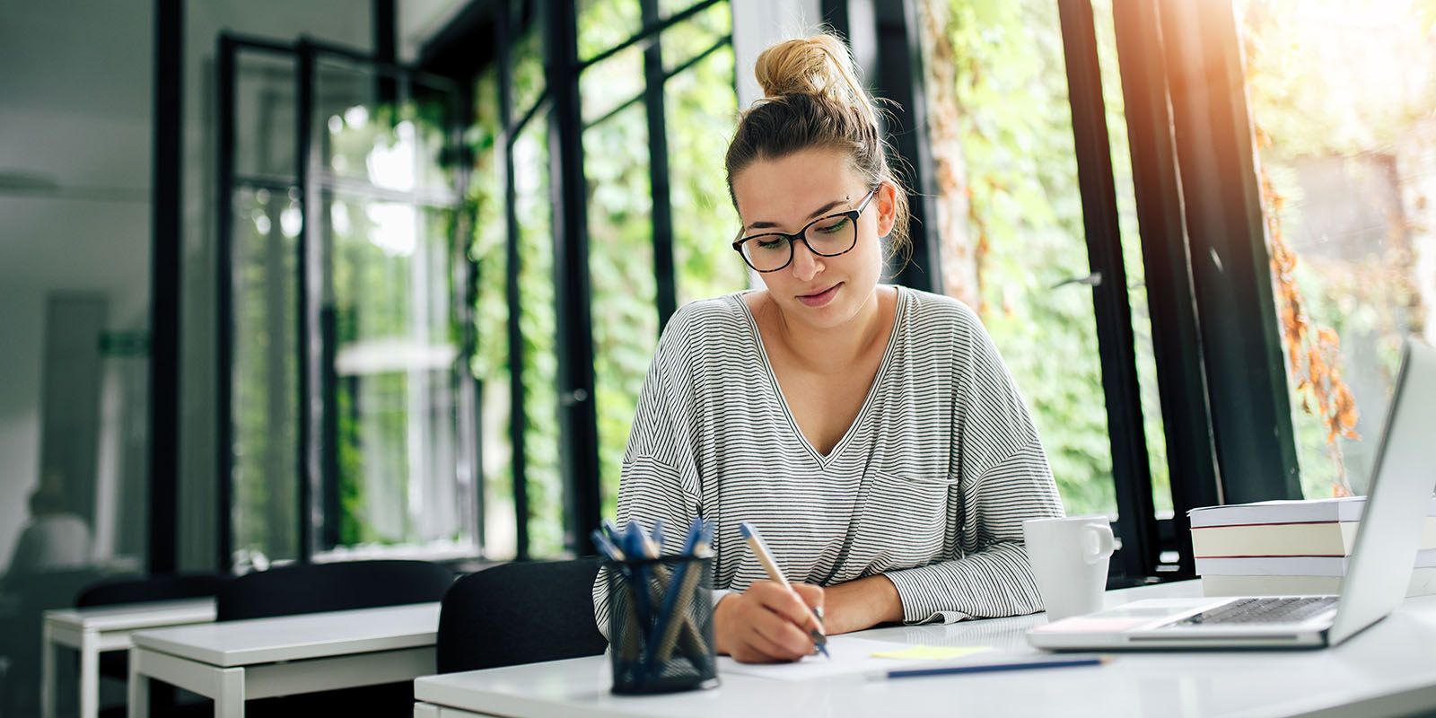 A female with glasses sitting at her desk writing