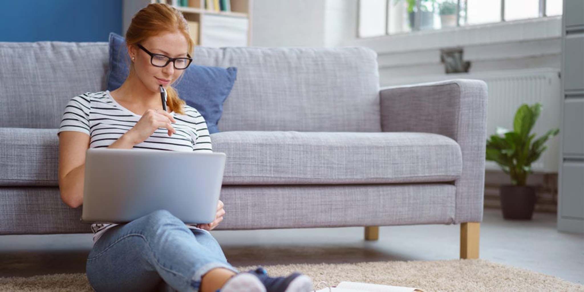 Female student leaning on grey couch with lap top studying