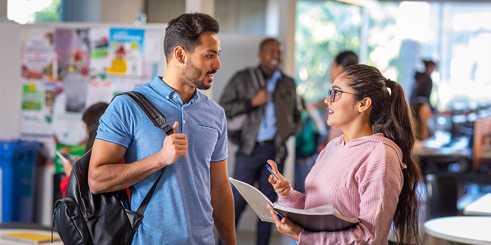 Two students standing outside a classroom, speaking English