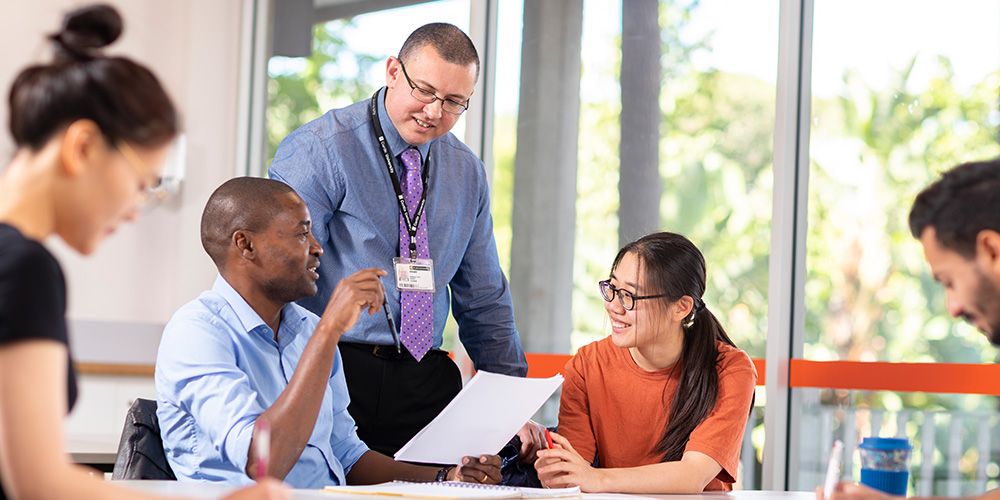 Two Curtin English students and lecturer discussing in a classroom