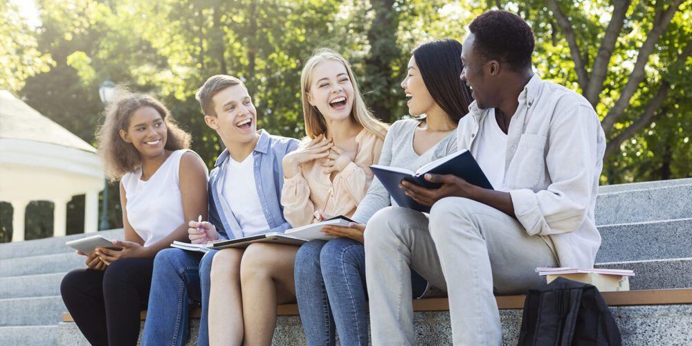 Multiracial students laughing outside and sitting on stairs