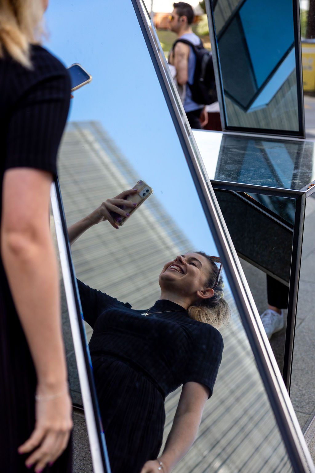 A student taking a selfie in the mirrored artwork on campus