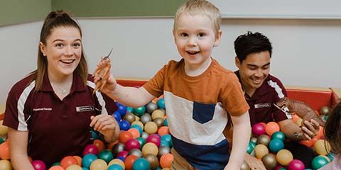 Both a male and female occupational therapy student in a ball pit with a small child