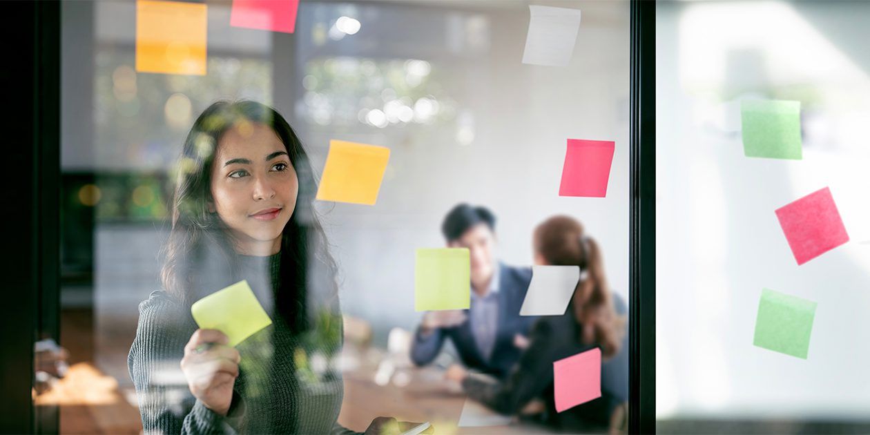 Female in an office setting placing post-its on a boardroom window