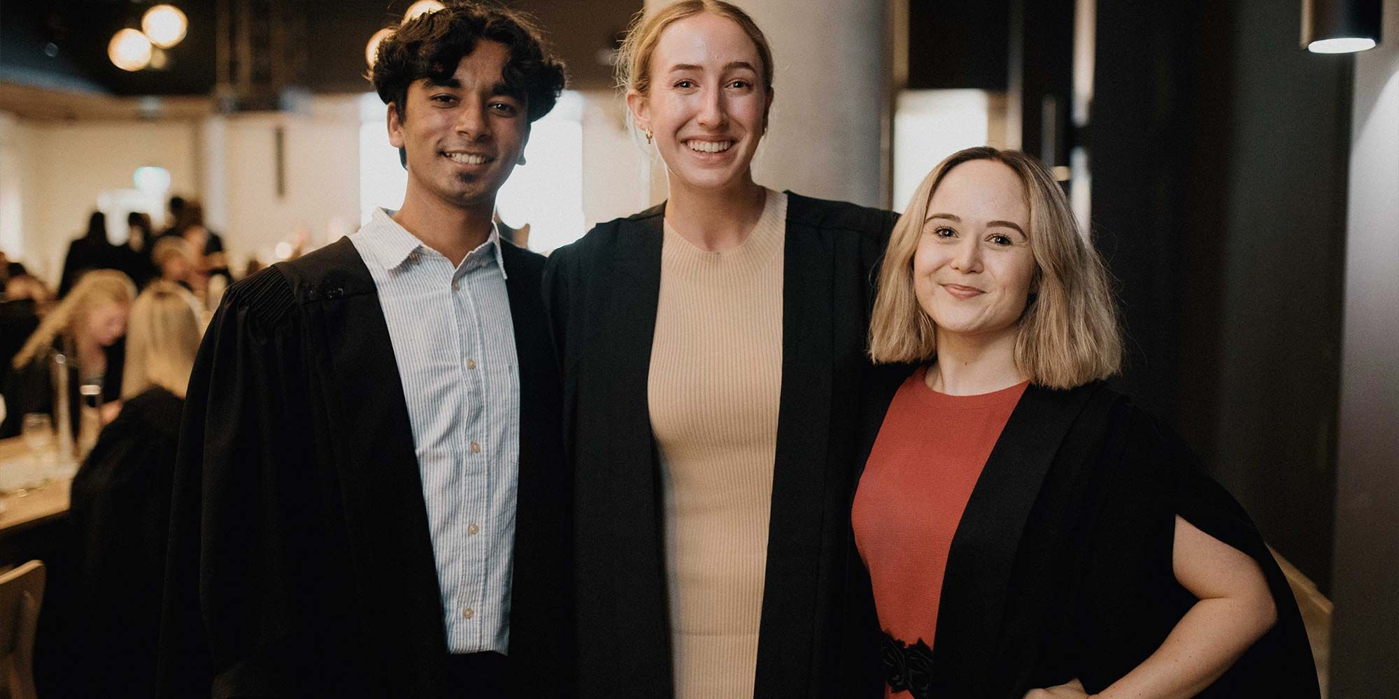 Three students wearing formal robes in the dining hall at St Catherine's College