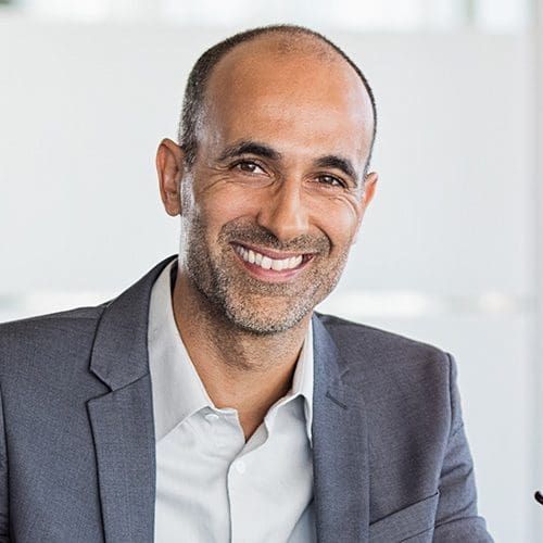 Happy mature business man holding spectacles in modern office. Successful senior businessman in formals sitting in meeting room with phone and tablet. Smiling man in suit in a elegant office.