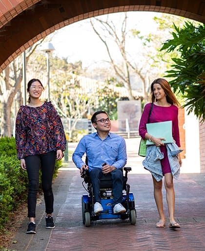 Two female students and a male student in wheelchair walking on Curtin campus