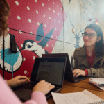 Male student smiling at female friend working on laptop