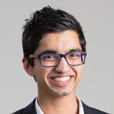 curtin student ryan soares wearing glasses and a suit standing against a dark green leafy background