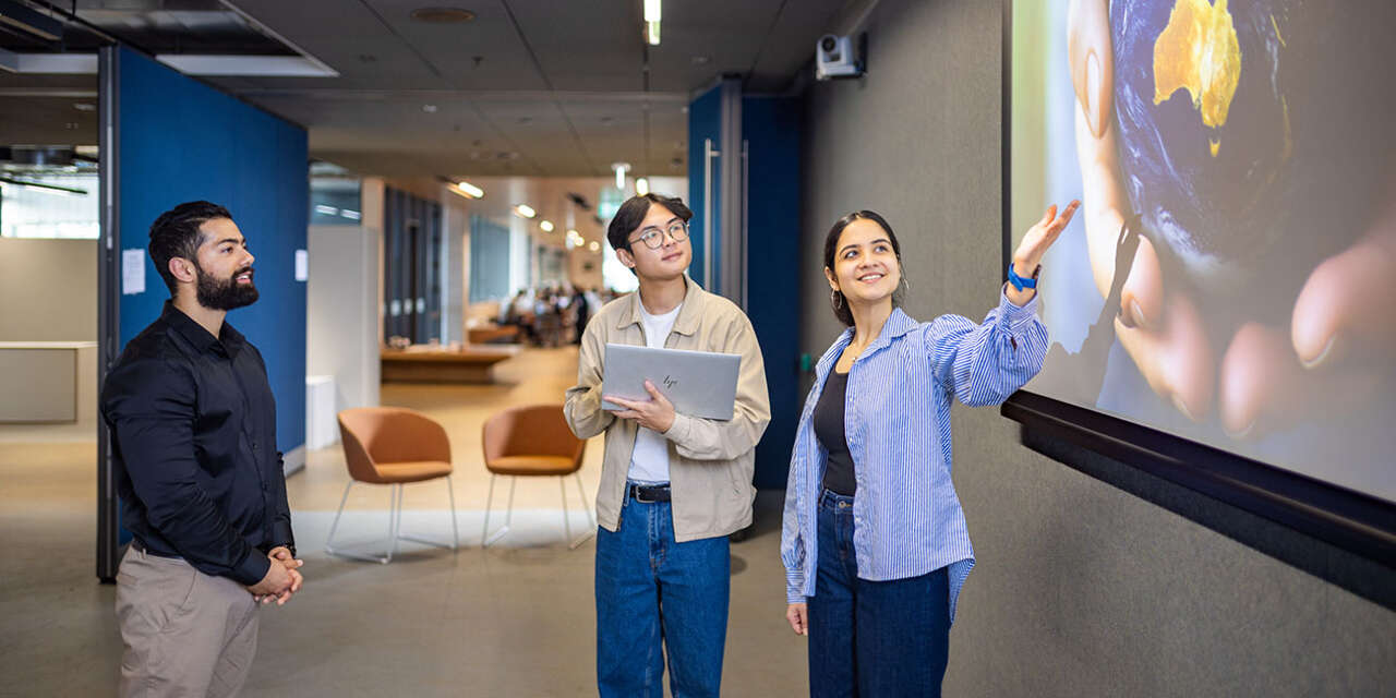 A young woman and two young men look happily at a projected image of the Earth.