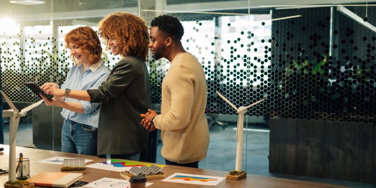 Three casually-dressed, smiling young professionals study information on a notebook computer