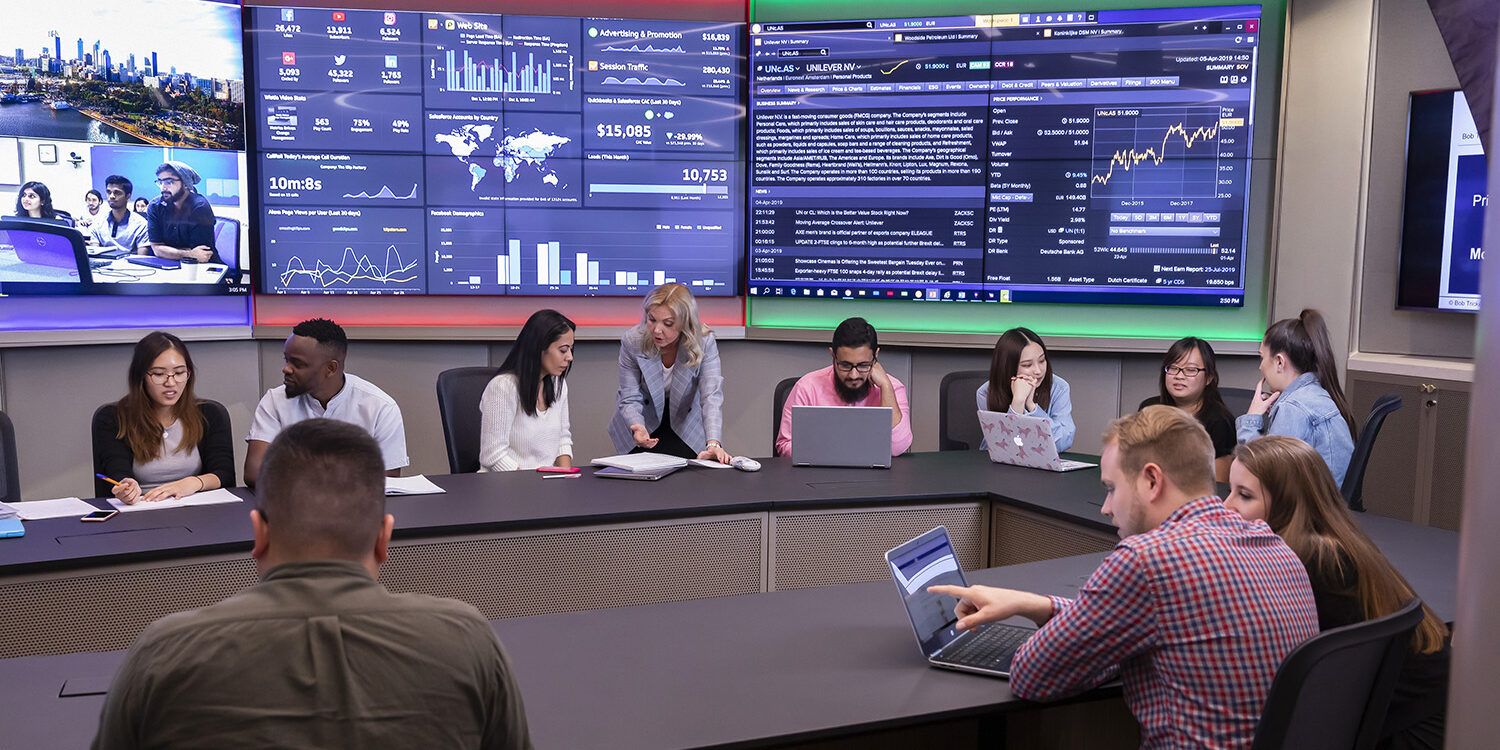 Several people sitting a room with screens in the background